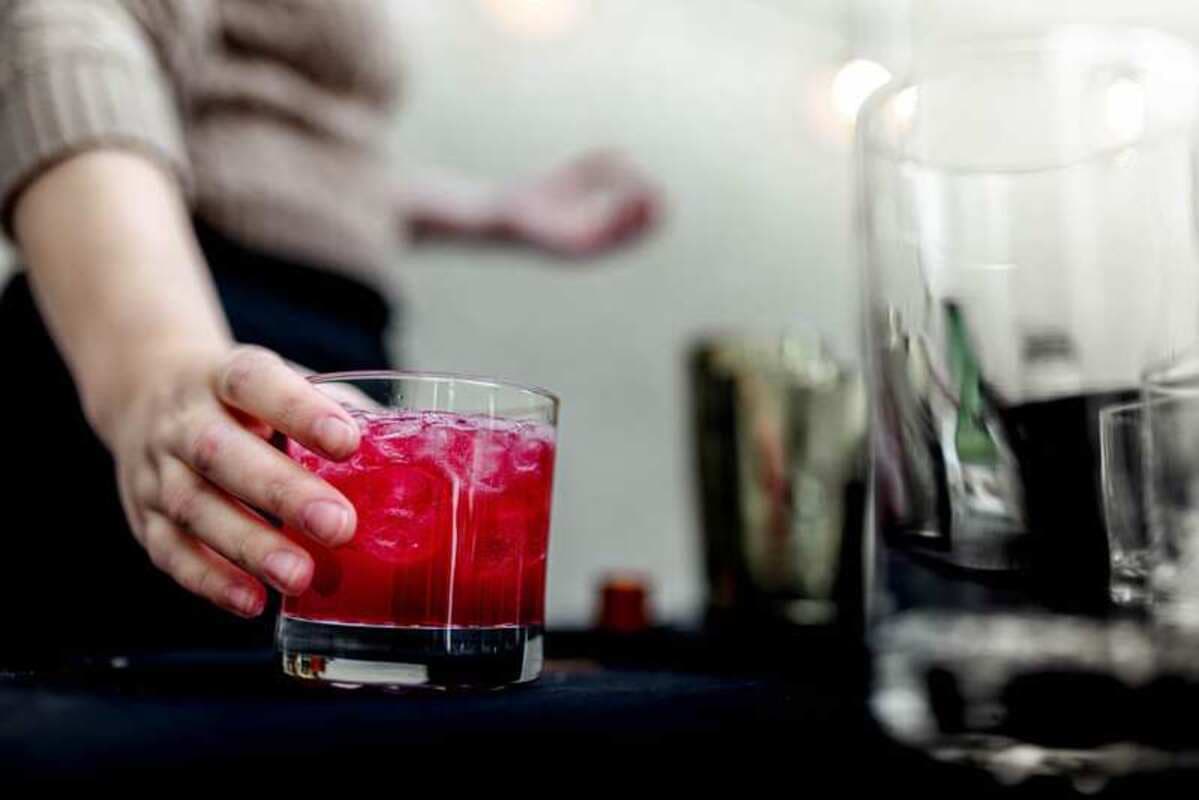 A bartender setting down a bright red cocktail on the bar